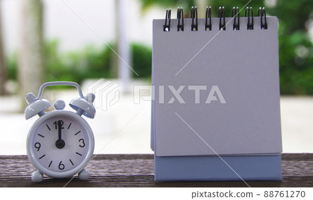 Alarm clock pointing at 12 o'clock with blank notepad. Blurred park background. Copy space Alarm clock pointing at 12 o'clock with blank notepad. Blurred park background. Copy space 88761270