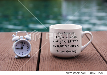 White alarm clock on wooden floor with morning quote text on coffee cup - It's a good day to start a good week. With blurred swimming pool background. 88761589