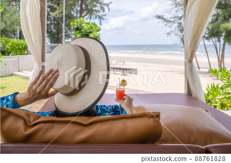 Asian woman relaxed on the beach with her red lime cherry cocktail in the hand in opening summer day 88761828