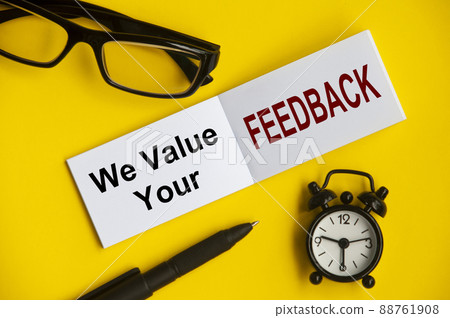Text on notepad with reading glasses, pen and alarm clock on yellow background - We value your feedback. Conceptual Text on notepad with reading glasses, pen and alarm clock on yellow background - We value your feedback. Conceptual 88761908