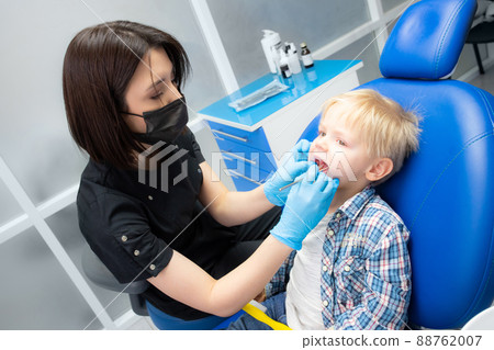 A cute little boy sits at the dentist, opened his mouth, showing his teeth to the dentist. Happy boy is sitting in the dentist's chair. Dentist - young brunette woman A cute little boy sits at the dentist, opened his mouth, showing his teeth to the dentist. Happy boy is sitting in the dentist's chair. Dentist - young brunette woman 88762007