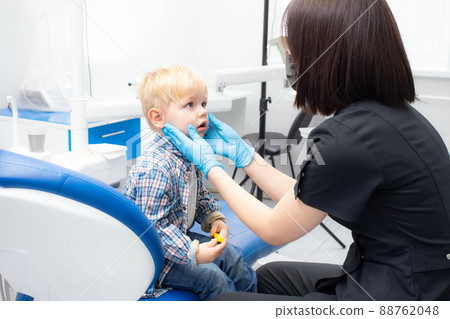 A cute little boy sits at the dentist, opened his mouth, showing his teeth to the dentist. Happy boy is sitting in the dentist's chair. Dentist - young brunette woman A cute little boy sits at the dentist, opened his mouth, showing his teeth to the dentist. Happy boy is sitting in the dentist's chair. Dentist - young brunette woman 88762048