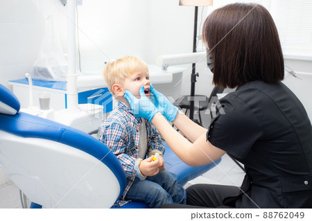 A cute little boy sits at the dentist, opened his mouth, showing his teeth to the dentist. Happy boy is sitting in the dentist's chair. Dentist - young brunette woman A cute little boy sits at the dentist, opened his mouth, showing his teeth to the dentist. Happy boy is sitting in the dentist's chair. Dentist - young brunette woman 88762049