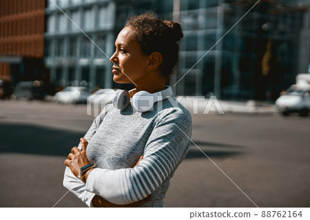 Thoughtful sporty woman looking away while standing outdoors in the daytime Thoughtful sporty woman looking away while standing outdoors in the daytime 88762164