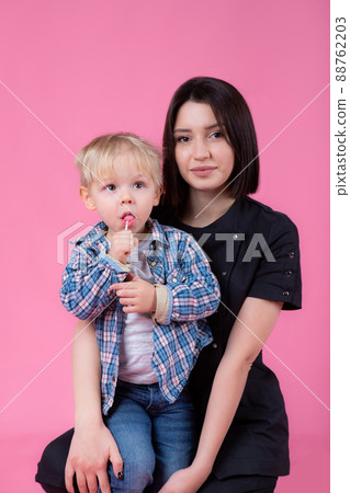 Young pediatrician woman with a cute little baby on a pink background. boy with candy Young pediatrician woman with a cute little baby on a pink background. boy with candy 88762203