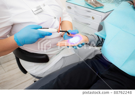 dental office. The dentist shows the child how the ultraviolet lamp works to harden the filling on the arm dental office. The dentist shows the child how the ultraviolet lamp works to harden the filling on the arm 88762248