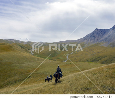 Riders with weapons on three horses move in mountainous terrain. 88762818