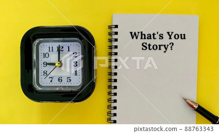 What is your story - message on white notebook. With alarm clock and yellow background. Business concept. 88763343