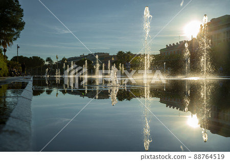 France, Nice, Famous place of Nice, square of fountain, mirror of water, playing kids, walking couples, a couple of old people are basking in the sunset, sun reflection, passing tram France, Nice, Famous place of Nice, square of fountain, mirror of water, playing kids, walking couples, a couple of old people are basking in the sunset, sun reflection, passing tram 88764519