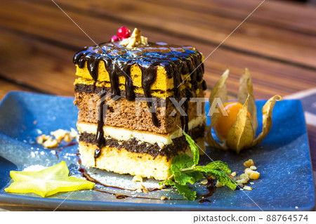 A delicious piece of sponge cake with a chocolate dripping down. Sweet dessert on blue plate. Beautiful serving of dish in cafe, restaurant. Plate with slice of tasty homemade chocolate cake on table. A delicious piece of sponge cake with a chocolate dripping down. Sweet dessert on blue plate. Beautiful serving of dish in cafe, restaurant. Plate with slice of tasty homemade chocolate cake on table. 88764574