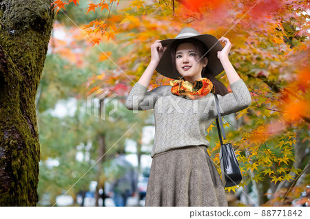 一個戴著帽子的微笑女人在秋天的花園裡漫步 88771842