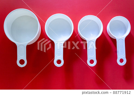 Set of white measuring cups, measuring spoons use in cooking lay on wooden red background in top view Set of white measuring cups, measuring spoons use in cooking lay on wooden red background in top view 88771912