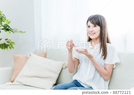 A woman eating yogurt on the sofa (smile) A woman eating yogurt on the sofa (smile) 88772121