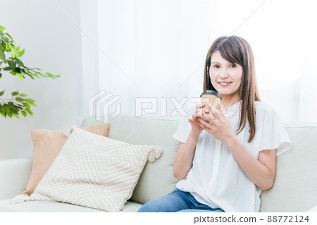 Middle-aged woman drinking a cup of coffee on the sofa Middle-aged woman drinking a cup of coffee on the sofa 88772124