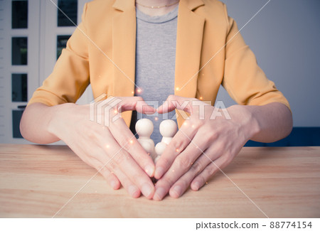 Woman's hands in the shape of a heart with a wooden doll inside. international day of families. hands protecting family. insurance, domestic violence, world mental health day, Family care concept. 88774154
