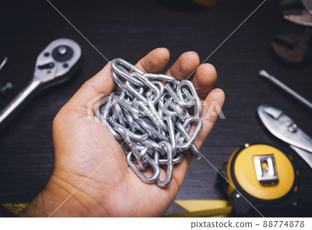A metal chain on the mechanic hand with a mechanic tools on wooden background A metal chain on the mechanic hand with a mechanic tools on wooden background 88774878