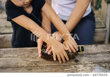 Close-up of little girl with her mom preparing cardboard for recycling. Family sorting garbage at home. Concept of recycling Close-up of little girl with her mom preparing cardboard for recycling. Family sorting garbage at home. Concept of recycling 88776459