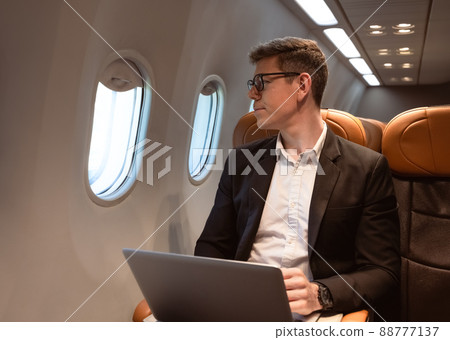 Businessman working with laptop while sitting in airplane seat and looking through aeroplane window. Business traveler concept. Businessman working with laptop while sitting in airplane seat and looking through aeroplane window. Business traveler concept. 88777137