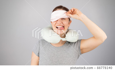 Smiling caucasian woman with a travel pillow takes off her sleep mask on a white background. 88778140