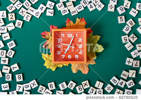 Orange alarm clock showing 7 am surrounded by math numbers on green background. Back to school concept. Flat lay. 88780820