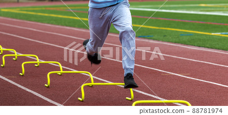 Legs of runner running over yellow mini hurdles on a track close up 88781974