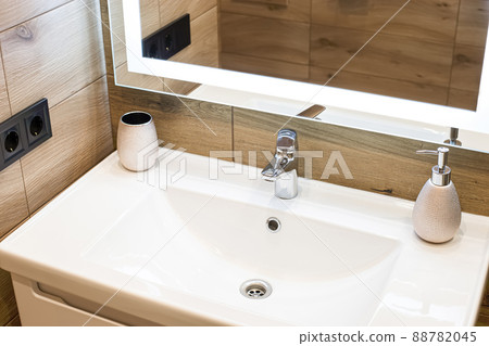 Modern washbasin with chrome faucet beside a stylish soap dispenser. 88782045