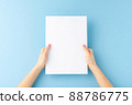 Young woman hands holding blank paper sheet on blue background. Mockup 88786775