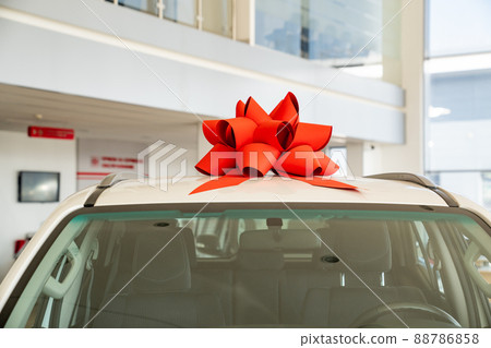 a red gift bow on the roof of a new white car in the car dealership.  88786858