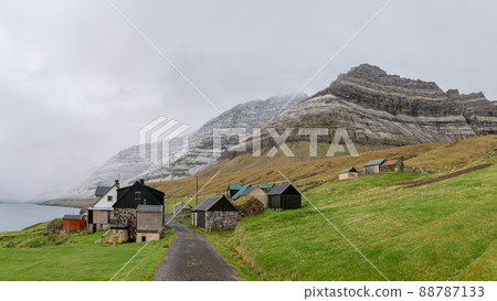 Bour, Faroe Islands - August 2019: A small settlement village overlooking a fjord surrounded by green and snowy mountains Bour, Faroe Islands - August 2019: A small settlement village overlooking a fjord surrounded by green and snowy mountains 88787133