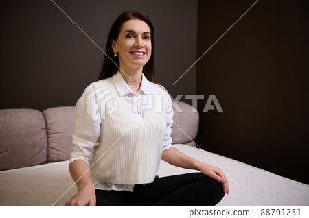 Attractive woman smiles sitting in lotus position on an orthopedic mattress in the exhibition hall of a furniture store 88791251