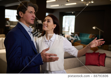 Handsome Caucasian man buying upholstered furniture in a furniture store, listening to the recommendations of the sales manager in the showroom Handsome Caucasian man buying upholstered furniture in a furniture store, listening to the recommendations of the sales manager in the showroom 88791606