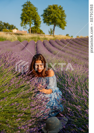 The beautiful young girl in a blue dress sits on the field of a lavender flowers, long curly hair, bright smile, a house of the gardener, trees, perspective of a lavender The beautiful young girl in a blue dress sits on the field of a lavender flowers, long curly hair, bright smile, a house of the gardener, trees, perspective of a lavender 88791988