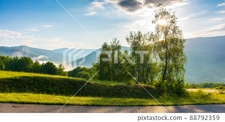 serpentine mountain road down the hill. trees meadow along the way. fog rising in the distant valley. sun above horizon. fluffy clouds on the sky. idyllic travel scenery on a summer morning serpentine mountain road down the hill. trees meadow along the way. fog rising in the distant valley. sun above horizon. fluffy clouds on the sky. idyllic travel scenery on a summer morning 88792359