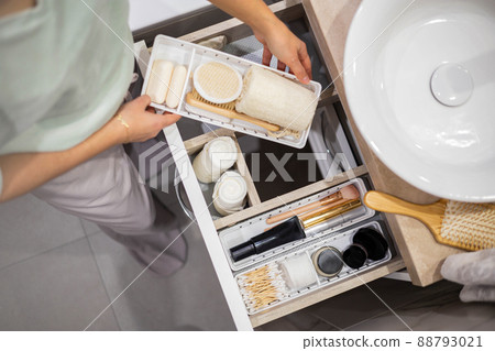 Top view of woman hands neatly organizing bathroom amenities and toiletries in drawer in bathroom. 88793021