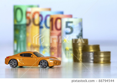 Blurred row of rolled hundred, fifty, twenty, ten and five new euro banknotes and pile of coins with yellow toy expensive sport car. Symbol of financial prosperity, vehicle sale and purchase. 88794544