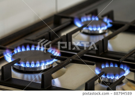 Natural gas burning on kitchen gas stove in the dark. Panel from steel with a gas ring burner on a black background, close-up shooting 88794589