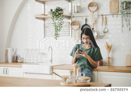 Happy young asian woman relaxing at home she is standing at counter kitchen Happy young asian woman relaxing at home she is standing at counter kitchen 88798974