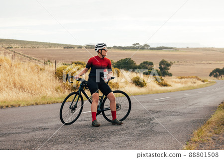 Pro bike female rider wearing helmet and sunglasses training outdoors on empty countryside road 88801508