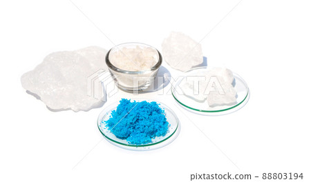 Closeup inorganic chemical on white laboratory table. Copper(II) sulfate in Chemical Watch Glass. Alum Crystal and Flake salt were placed further away. Closeup inorganic chemical on white laboratory table. Copper(II) sulfate in Chemical Watch Glass. Alum Crystal and Flake salt were placed further away. 88803194