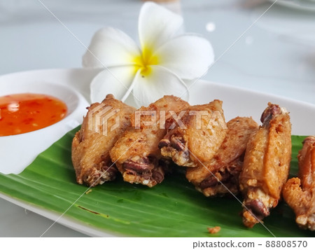 Fried chicken wings on a plate with rests and a cup of dipping sauce 88808570