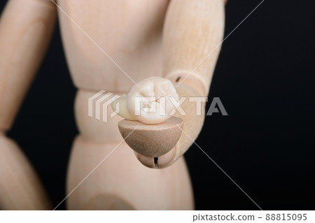 Human wooden figure holds in hand extracted human tooth on a black background. 88815095