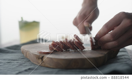 Man slicing mini salami sausage on wood board Man slicing mini salami sausage on wood board 88818544
