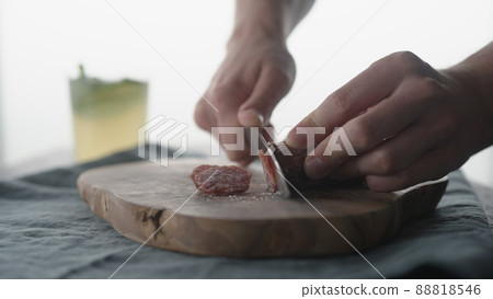 Man slicing mini salami sausage on wood board Man slicing mini salami sausage on wood board 88818546