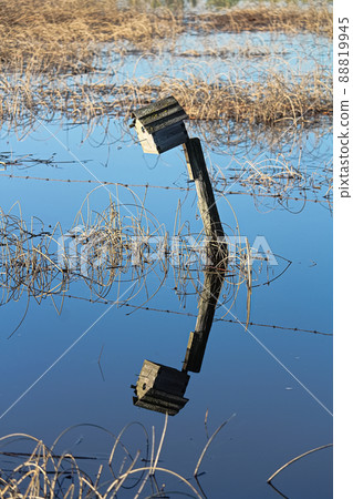A birdhouse on a fence with its reflection in water 88819945