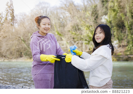 Earth Day concept, Woman and daughter pick up garbage in litter bags, clean-ups in nature to recycling in their communities, clean river and protect environment from pollution, conservation Nature. Earth Day concept, Woman and daughter pick up garbage in litter bags, clean-ups in nature to recycling in their communities, clean river and protect environment from pollution, conservation Nature. 88821223
