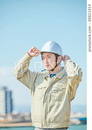 A young man in work clothes wearing a helmet against the blue sky 88821914