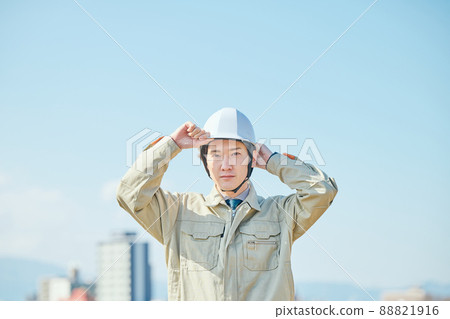 A young man in work clothes wearing a helmet against the blue sky A young man in work clothes wearing a helmet against the blue sky 88821916