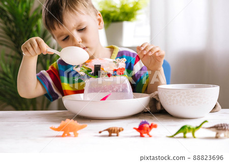 A cute little child pours warm water over toys frozen in ice. Dinosaur defrosting. Early development 88823696
