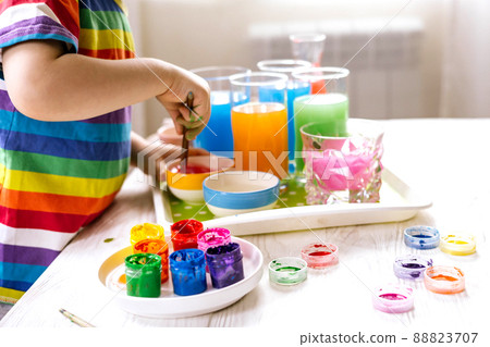 Cute baby boy learning mixing different colors with water and paint in containers. Early development 88823707