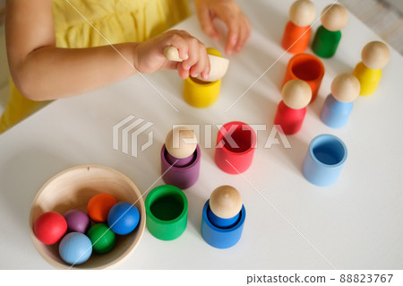 Child throws a yellow ball into a cup of the appropriate color with a spoon. Educational game - sort figures by colors. Wooden Multicolored Developmental Toy for Preschoolers Child throws a yellow ball into a cup of the appropriate color with a spoon. Educational game - sort figures by colors. Wooden Multicolored Developmental Toy for Preschoolers 88823767